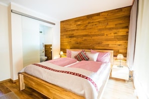 A modern hotel room with a wooden headboard, a large bed with red and white bedding, a bedside table with a lamp, and a sliding door closet.