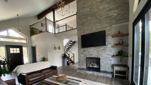 Ein geräumiges Wohnzimmer mit Kamin aus Stein, einem großen Fernseher und einer Treppe, die in einen oberen Bereich führt.