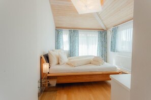 A room with a wooden ceiling, a bed with white bedding, and a window with curtains. - Offers space for up to 8 people Chalet Solymont by MoniCare in a quiet and sunny location (Seefeld)