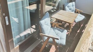Un balcón con puerta de cristal, una mesa de madera y dos sillas estampadas.