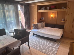 Een gezellige kamer met een bed, een bureau en een stoel. Er is een raam met gordijnen, een plank met boeken en een wandlamp.