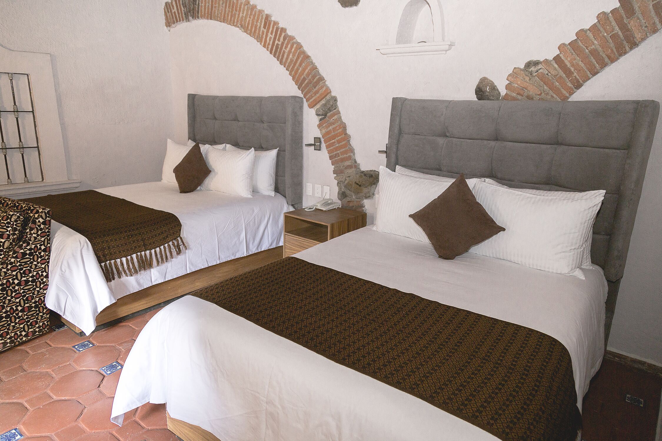 A room with two beds, each with a headboard, a nightstand, and a telephone.