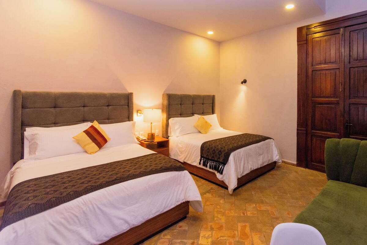 A hotel room with two beds, a green armchair, a wooden door, and a tiled floor.