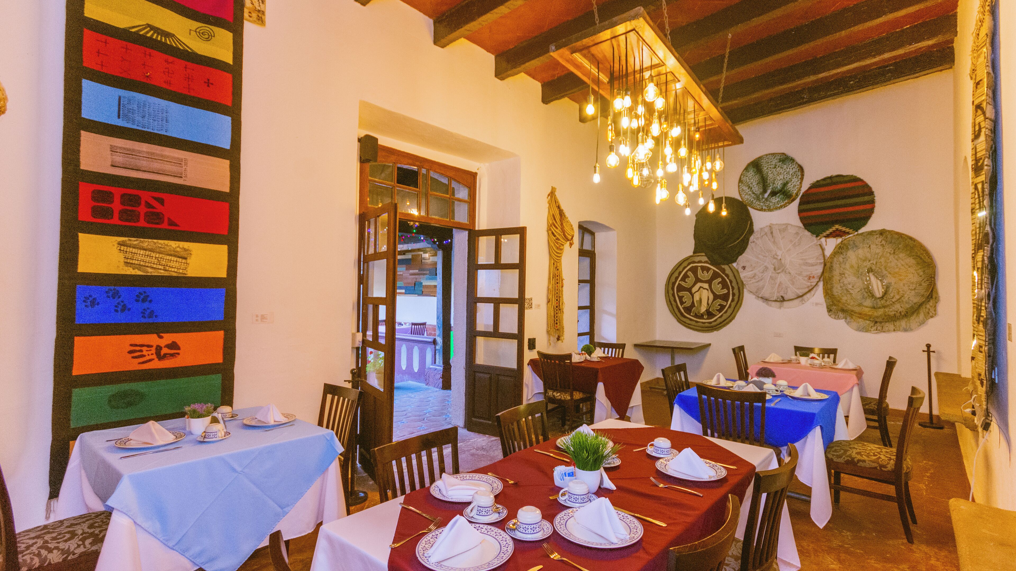 Un restaurant avec des tables dressées pour le service, un lustre et des éléments décoratifs accrochés aux murs.