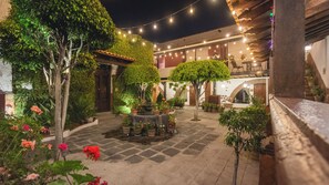 Un patio con plantas en macetas, una mesa central y luces colgantes.