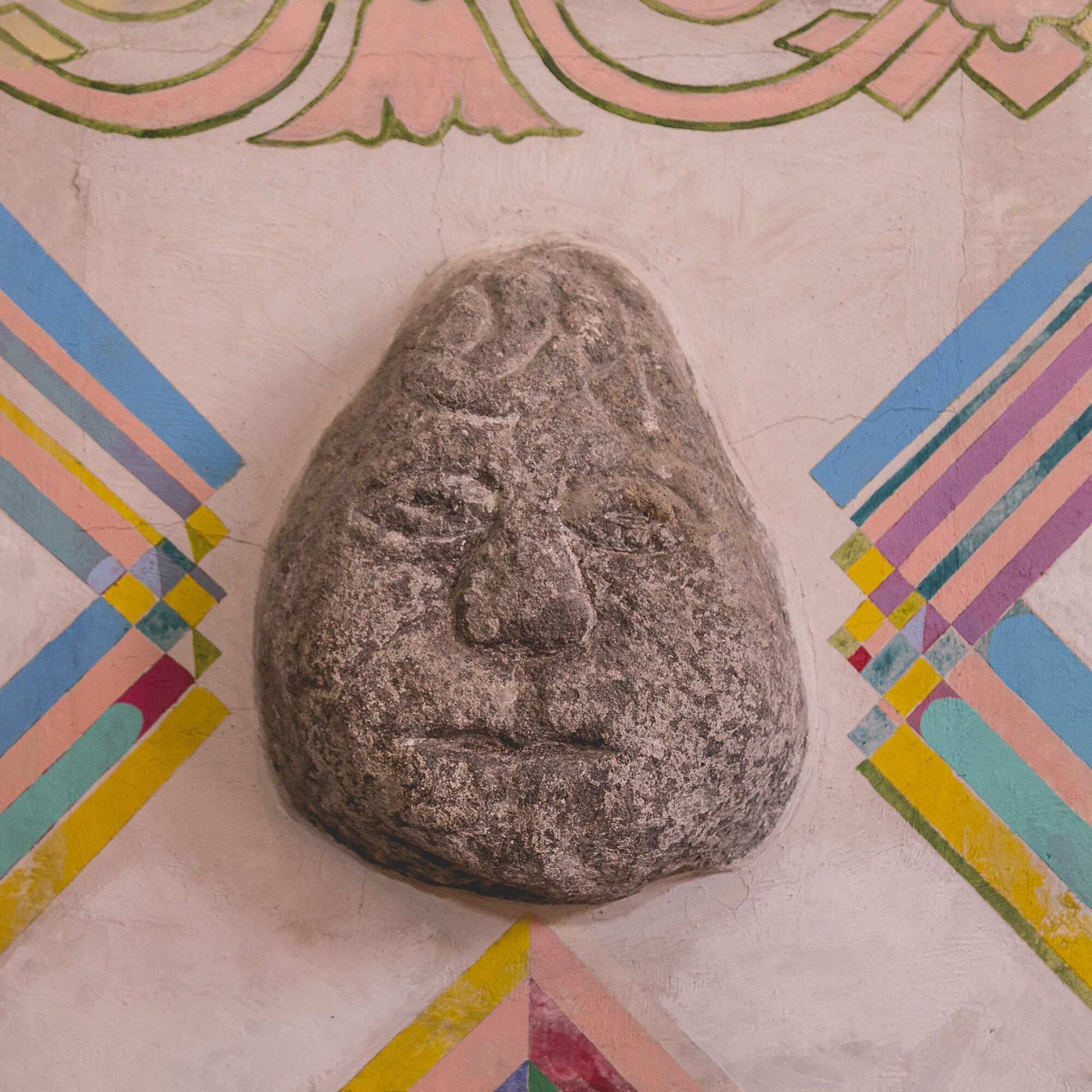 A stone with a carved face on a wall with colorful geometric patterns.