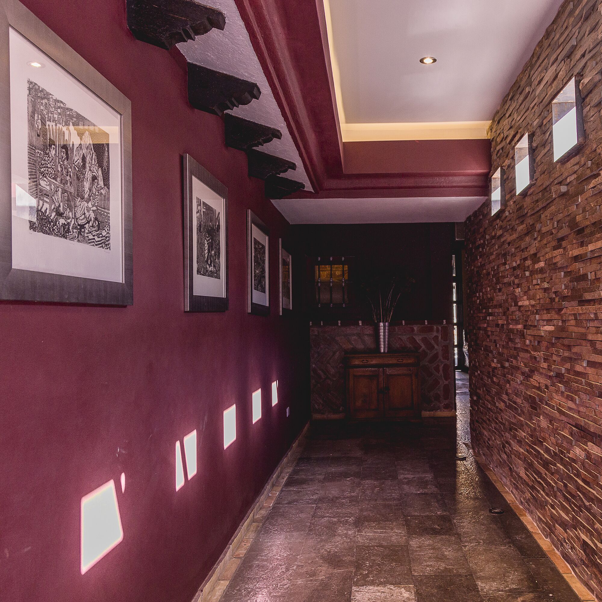 A hallway with framed pictures on the walls, a stone wall on one side, and a wooden cabinet in the background.