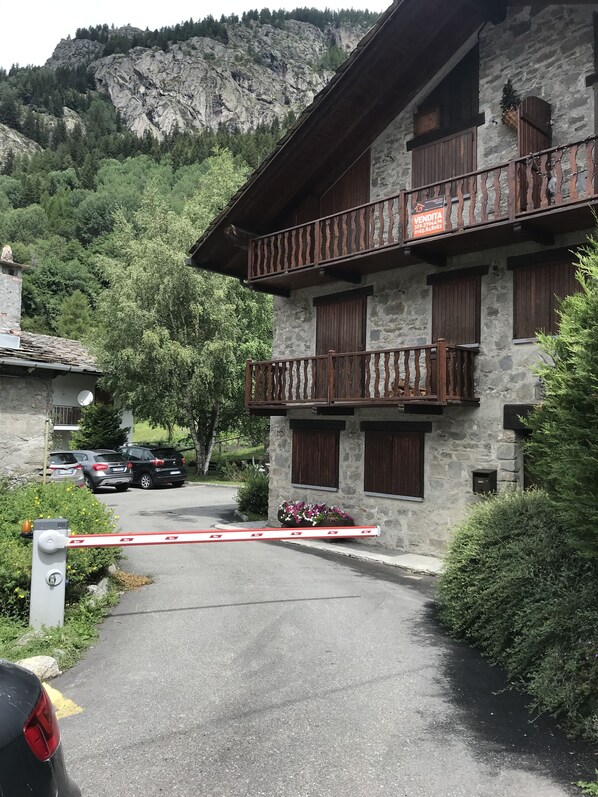 A stone building with a balcony, a gated driveway, and parked cars.