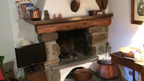 A cozy room with a stone fireplace, a television, and a wooden table with a bowl and a candle. - Fascinating views of Mont Blanc (Courmayeur)