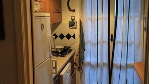 A compact kitchen with a refrigerator, stove, and cabinets. A curtain hangs in front of a door, and a small table is visible to the right. - Fascinating views of Mont Blanc (Courmayeur)
