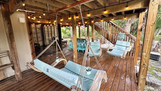 Eine Holzterrasse mit Hängestühlen und einem Tisch, umgeben von Holzbalken und Lichterketten.