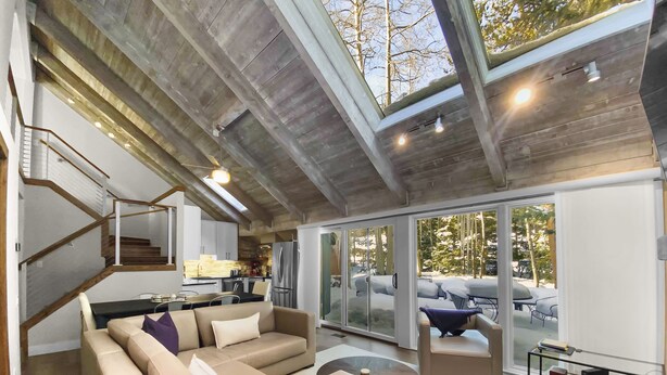 Ett rymligt vardagsrum med modern design, inrett med en stor soffa, ett soffbord och en glasdörr som leder ut till en utomhusplats med sittmöbler.