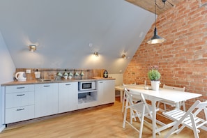 A kitchen with white cabinets, a wooden countertop, and a dining area with white chairs and a table. - Cosy Apartment in the ❤ of Old Town (Gdańsk)