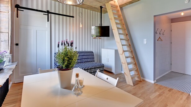 Ein modernes Interieur mit Esstisch, Sofa, Wand-Fernseher und einer Holzleiter.