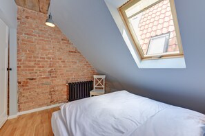 Camera da letto con soffitto spiovente, parete in mattoni a vista, un lucernario, un termosifone e un letto con biancheria da letto bianca.