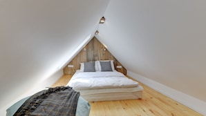 Ein kleines, dreieckiges Schlafzimmer im Dachgeschoss mit Holzbalken, einem Bett mit weißer Bettwäsche und zwei Wandleuchten.