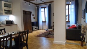 A modern living room with a grey sofa, wooden floor, and a dining area with a table and chairs.