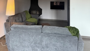 A modern living room with a grey sectional sofa, a black fireplace, a floor lamp, and a flat-screen TV mounted on the wall. - Villa in Provence (Cavaillon)