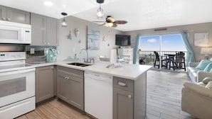A modern kitchen with a central island, a dining area with a view, and a balcony with outdoor seating. - Gulf Shores Plantation-Palms 6508 (Gulf Shores)