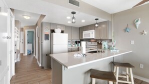 A modern kitchen with a central island, bar stools, and a microwave. - Gulf Shores Plantation-Palms 6508 (Gulf Shores)