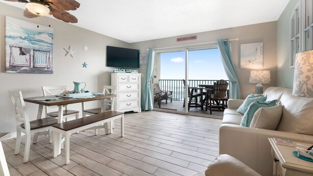 A spacious living room with a wooden floor, a white sofa, a dining table with chairs, and a ceiling fan. - Gulf Shores Plantation-Palms 6508 (Gulf Shores)