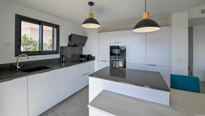A modern kitchen with a central island, white cabinetry, and pendant lighting. - Villa U Cousiu (Sainte Lucie De Porto Vecchio)