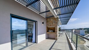 A balcony with a glass door leading to a room, a stone fireplace, and a view of the landscape. - Villa U Cousiu (Sainte Lucie De Porto Vecchio)