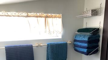 Un espace dédié à la buanderie, avec un étendoir où sont pliées les serviettes, un banc et une fenêtre avec des rideaux.