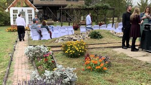 Een bruiloftlocatie in een tuin met witte stoelen, een houten constructie en diverse bloemen.