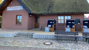 Tiilestä rakennettu rakennus, jossa on olkikatto, ja sen edessä on kyltti, jossa lukee ”Peenhaus Cafe & mehr”, sekä kaksi puista penkkiä.