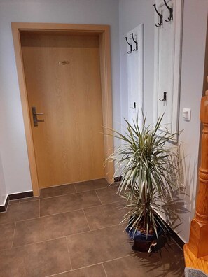A wooden door with a metal handle, a potted plant in the corner, and a white wall with a door handle and a light switch. - Vacation on the Peenestrom (Neukalen)