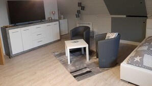 Moderni olohuone, jossa on sohva, sohvapöytä ja televisio, joka on sijoitettu kaappiin.