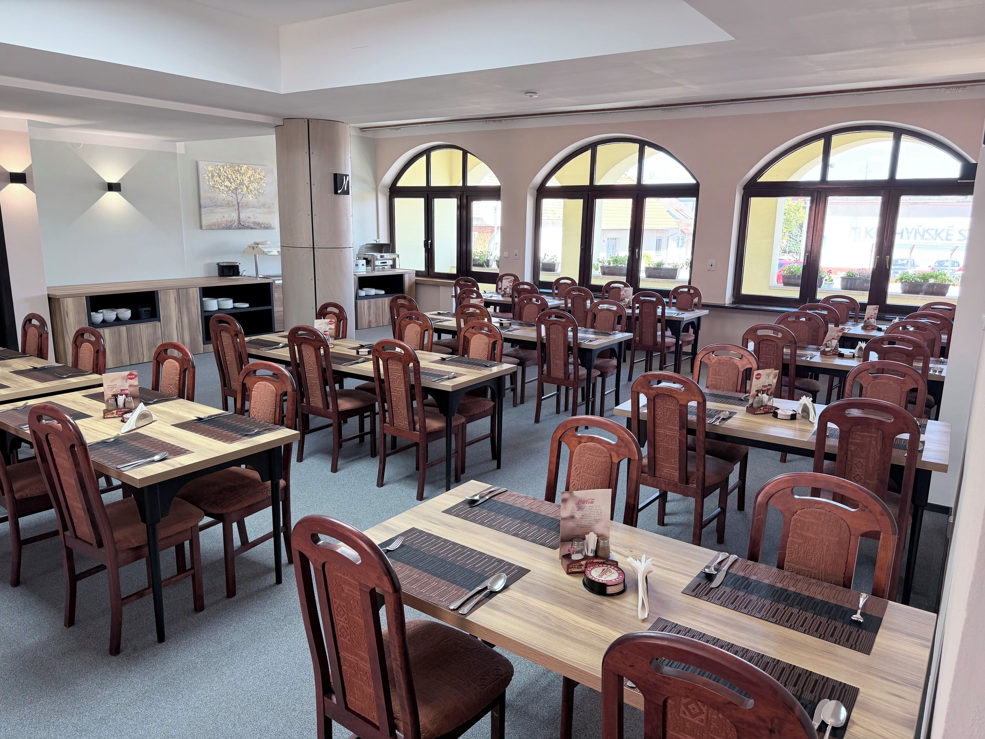 A spacious dining area with multiple tables and chairs, large arched windows, and a modern interior design.