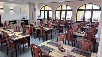 A spacious dining area with multiple tables and chairs, large arched windows, and a modern interior design.