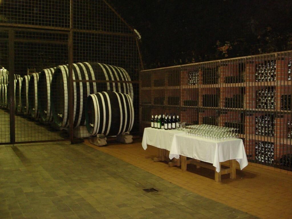 Una bodega con hileras de barricas de vino y una mesa con botellas y copas de vino.
