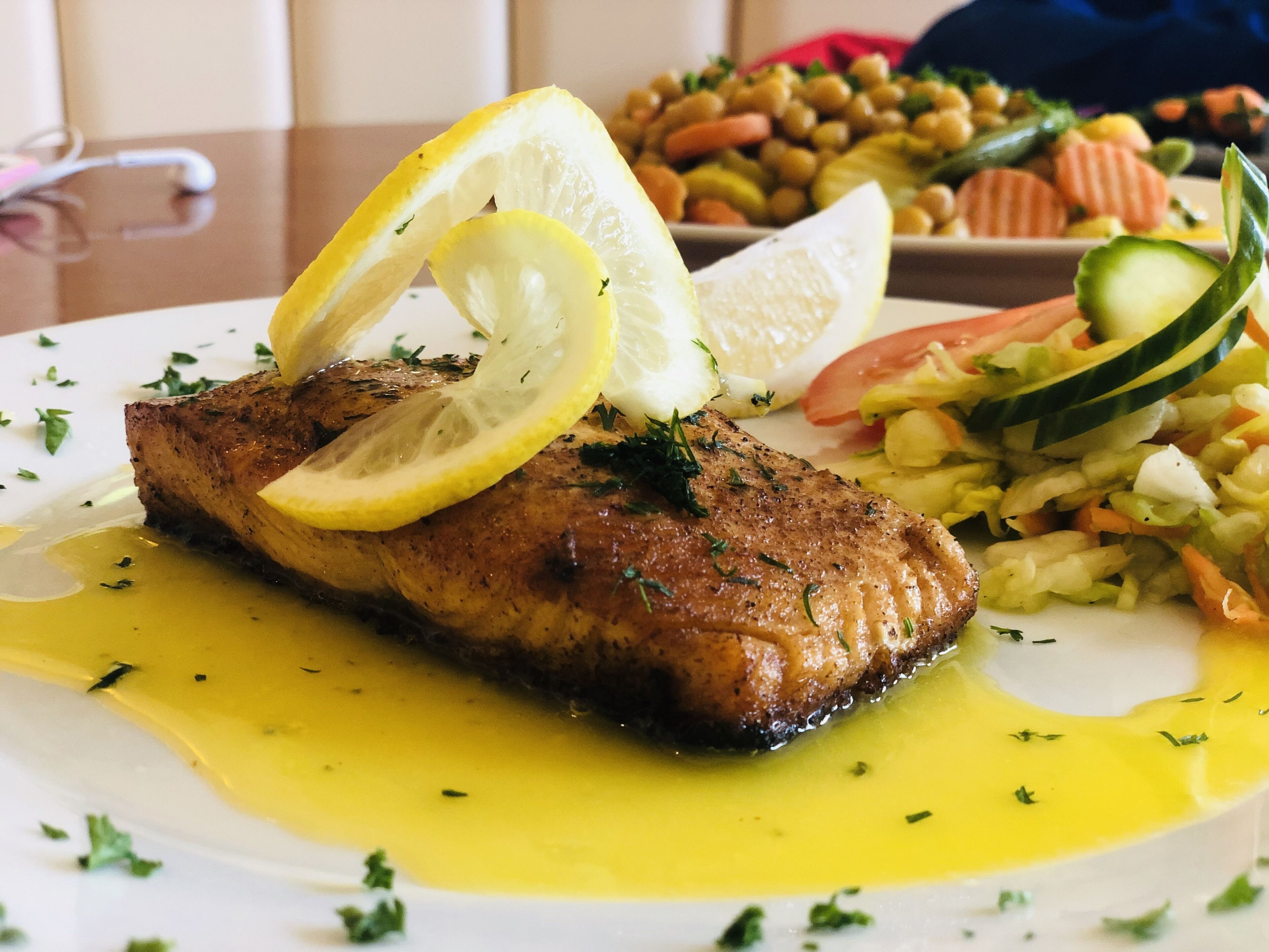 Un plato con pescado a la plancha, rodajas de limón y una ensalada.