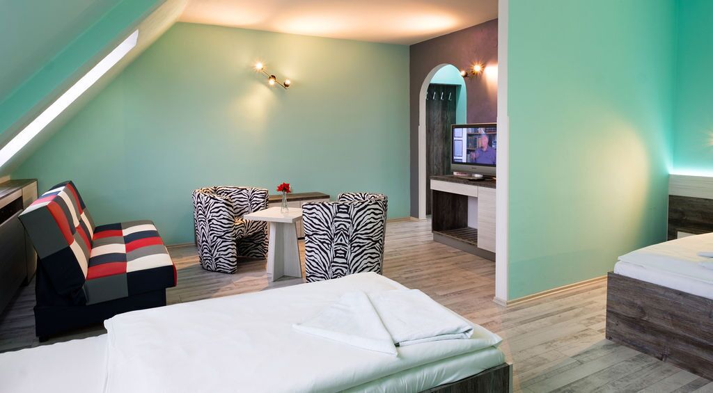 Una habitación moderna con cama, una pequeña mesa con sillas, televisor y kitchenette.