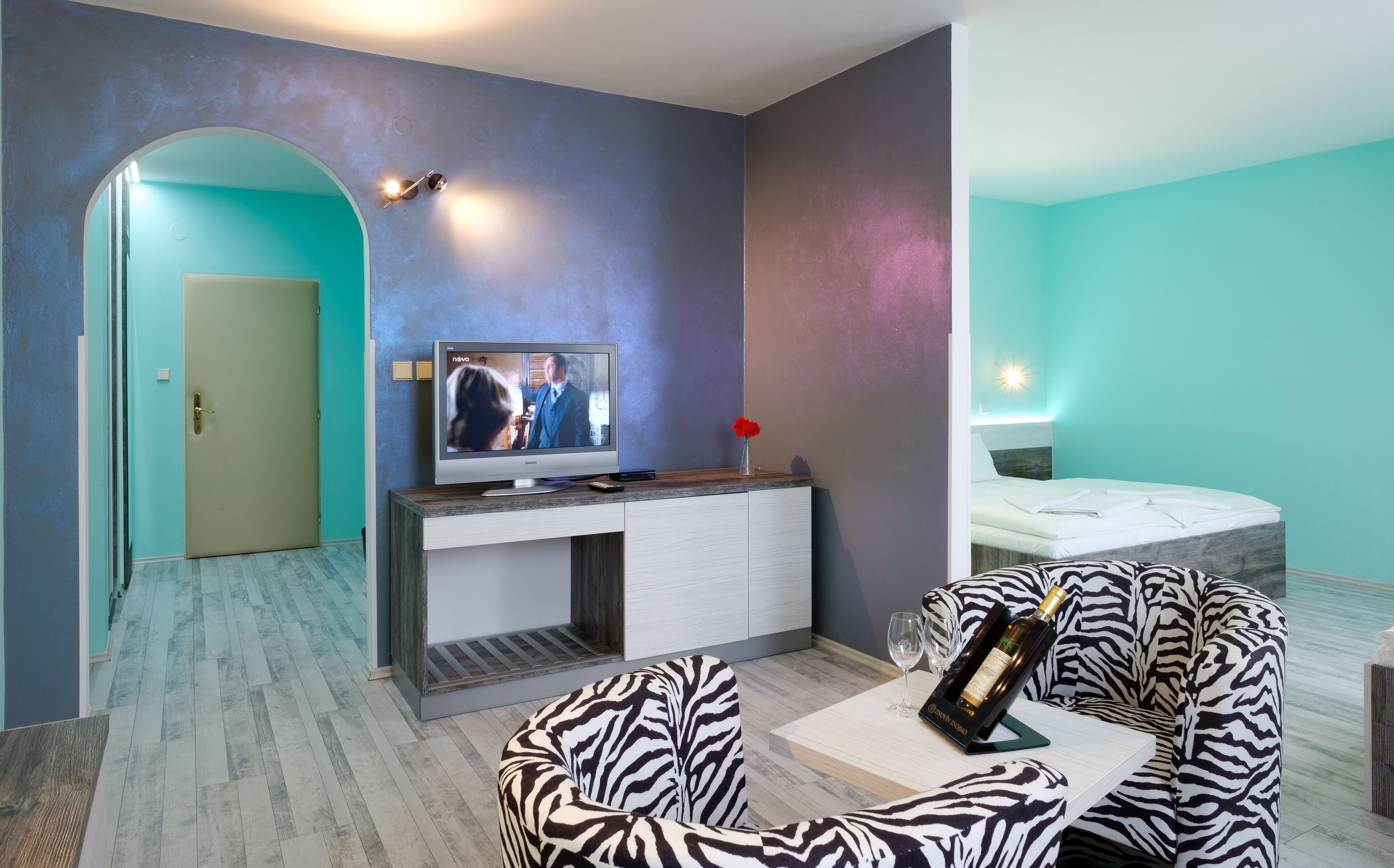 Une chambre d’hôtel moderne équipée d’une télévision, d’un canapé à motifs zébrés, d’un lit et d’une petite table sur laquelle se trouve une bouteille de vin.