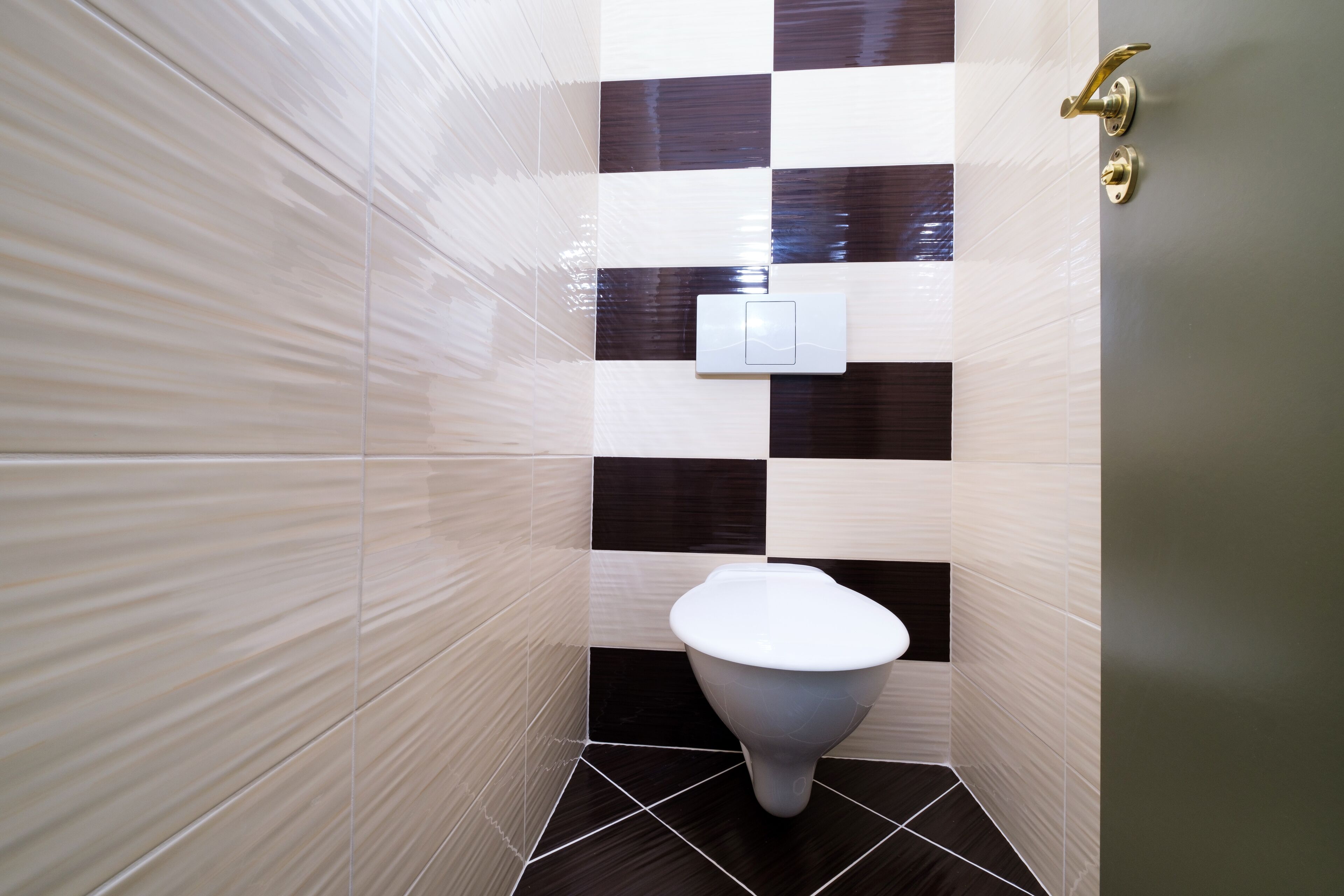 A bathroom with a white toilet, checkered black and white tiles, and a gold door handle.