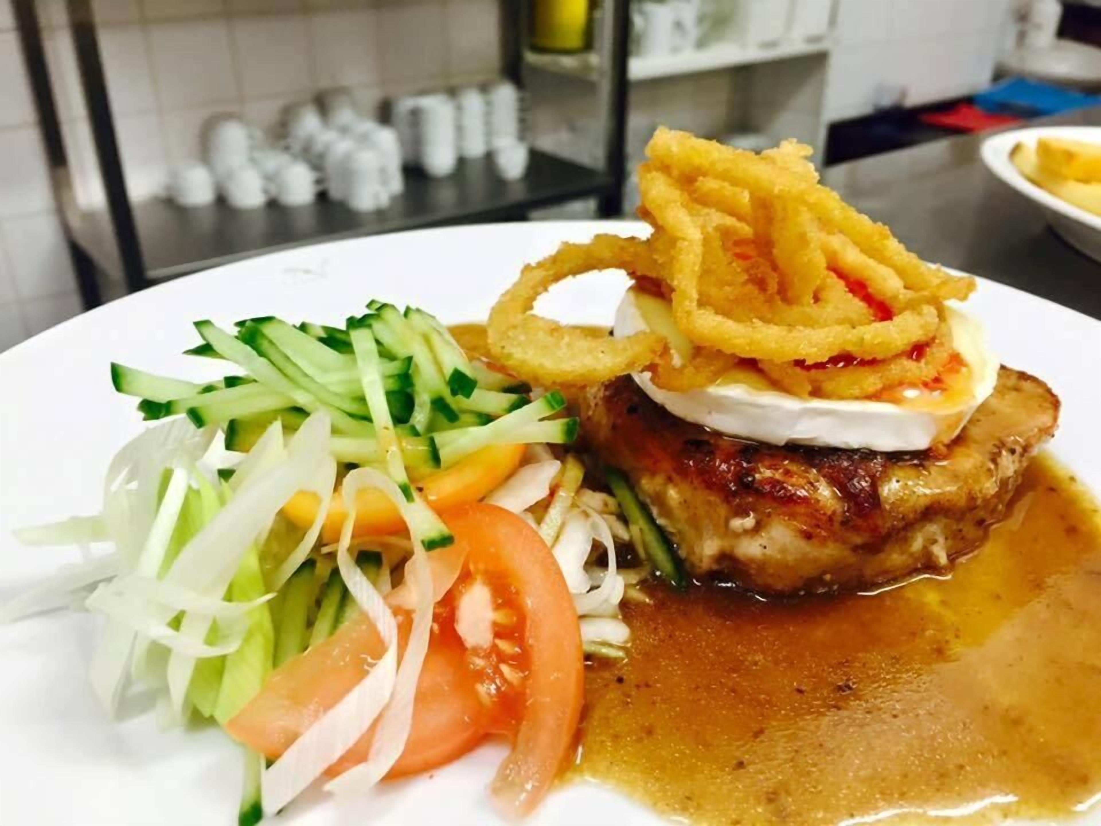 A plate with a grilled meat topped with onion rings, a side salad, and a sauce.