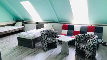 A room with a sloped ceiling, a bed, two zebra-patterned chairs, a small table, and a colorful sofa.