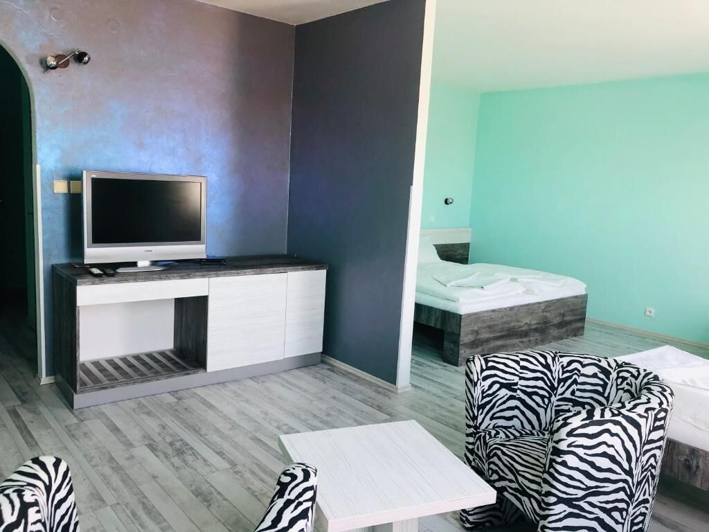 Una habitación moderna con un escritorio gris y blanco, un televisor de pantalla plana, una cama con colchón blanco y sillas con estampado de cebra.