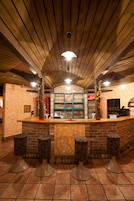Zona de bar con techo de madera, paredes de ladrillo y una barra con taburetes.