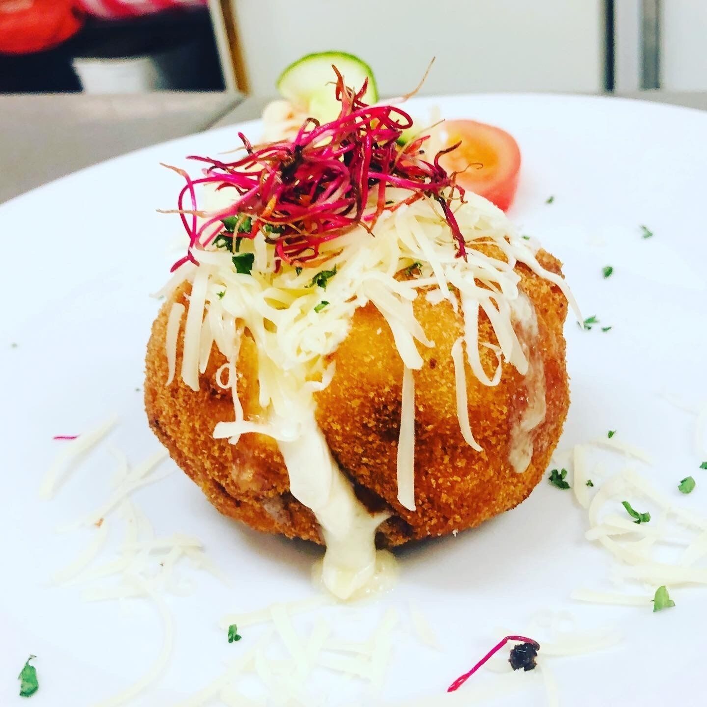 A dish with shredded vegetables, a slice of tomato, and a dollop of sauce on a white plate.