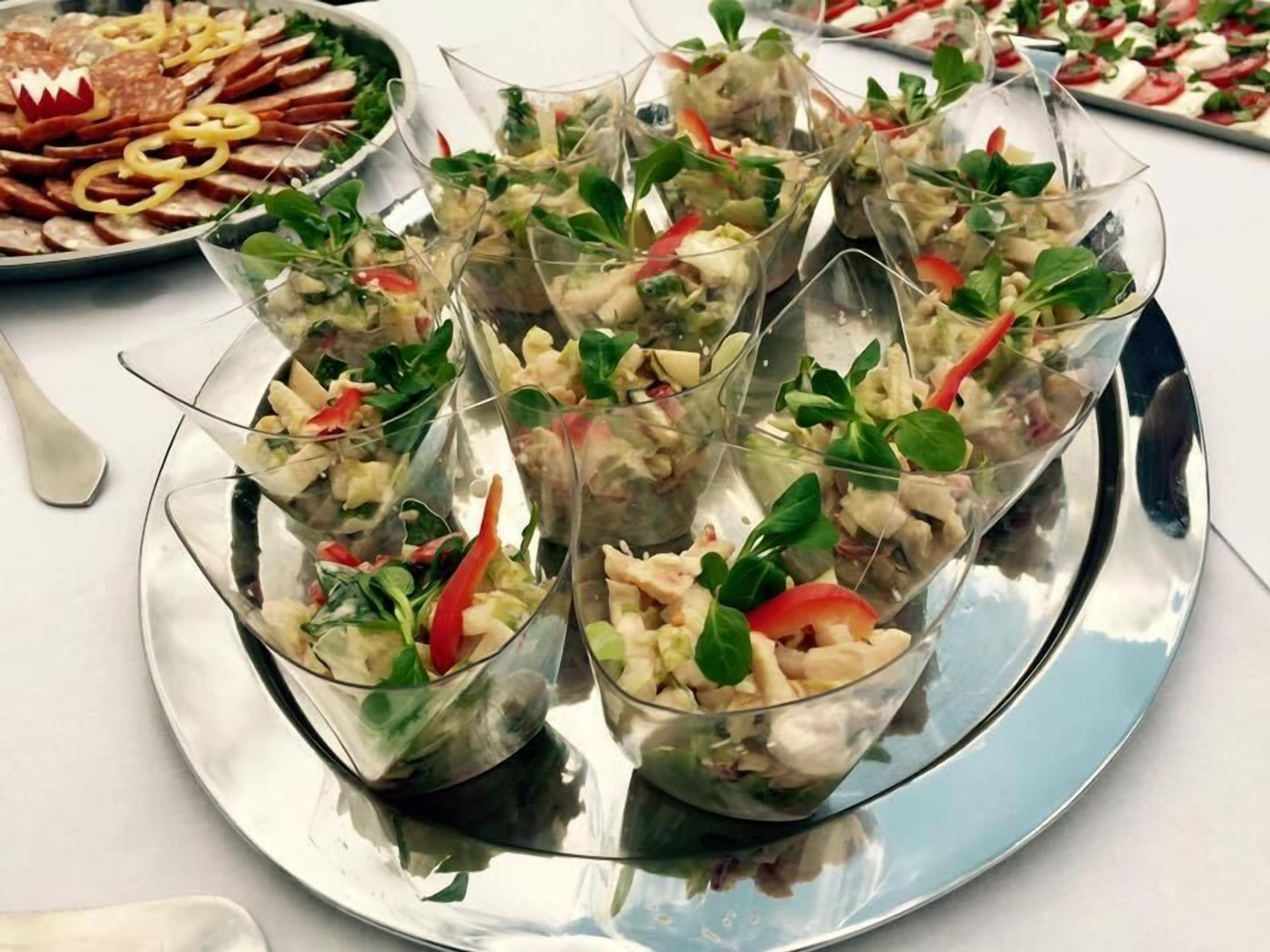 A tray of food consisting of various appetizers, including a salad with greens and tomatoes, and other mixed dishes.