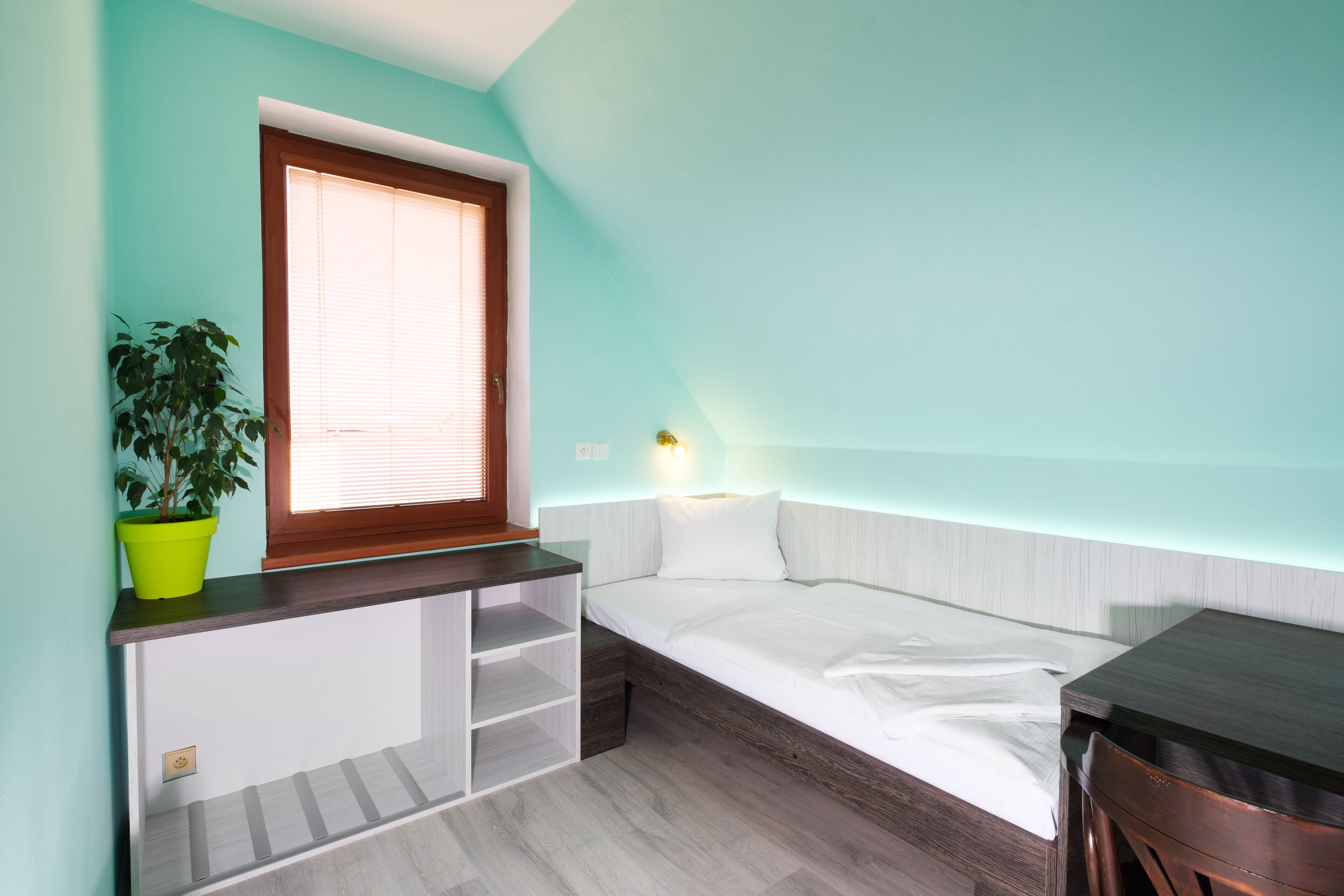 Un dormitorio con cama, ventana, escritorio y planta.