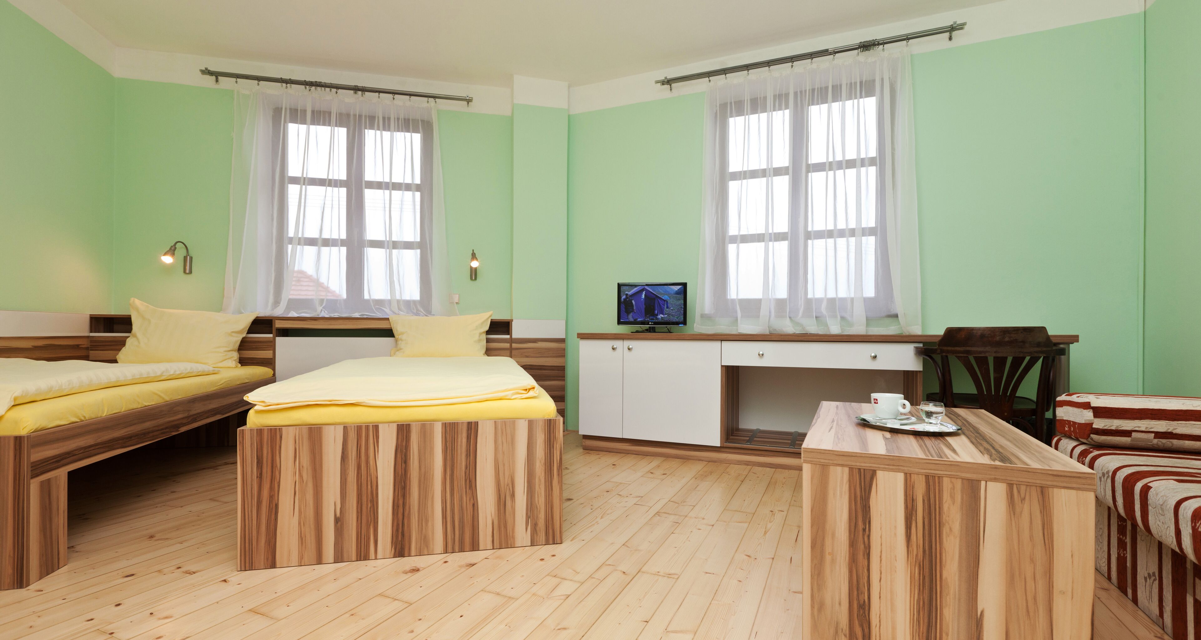 A room with two wooden beds, a small kitchenette, and a seating area with a table and chairs.