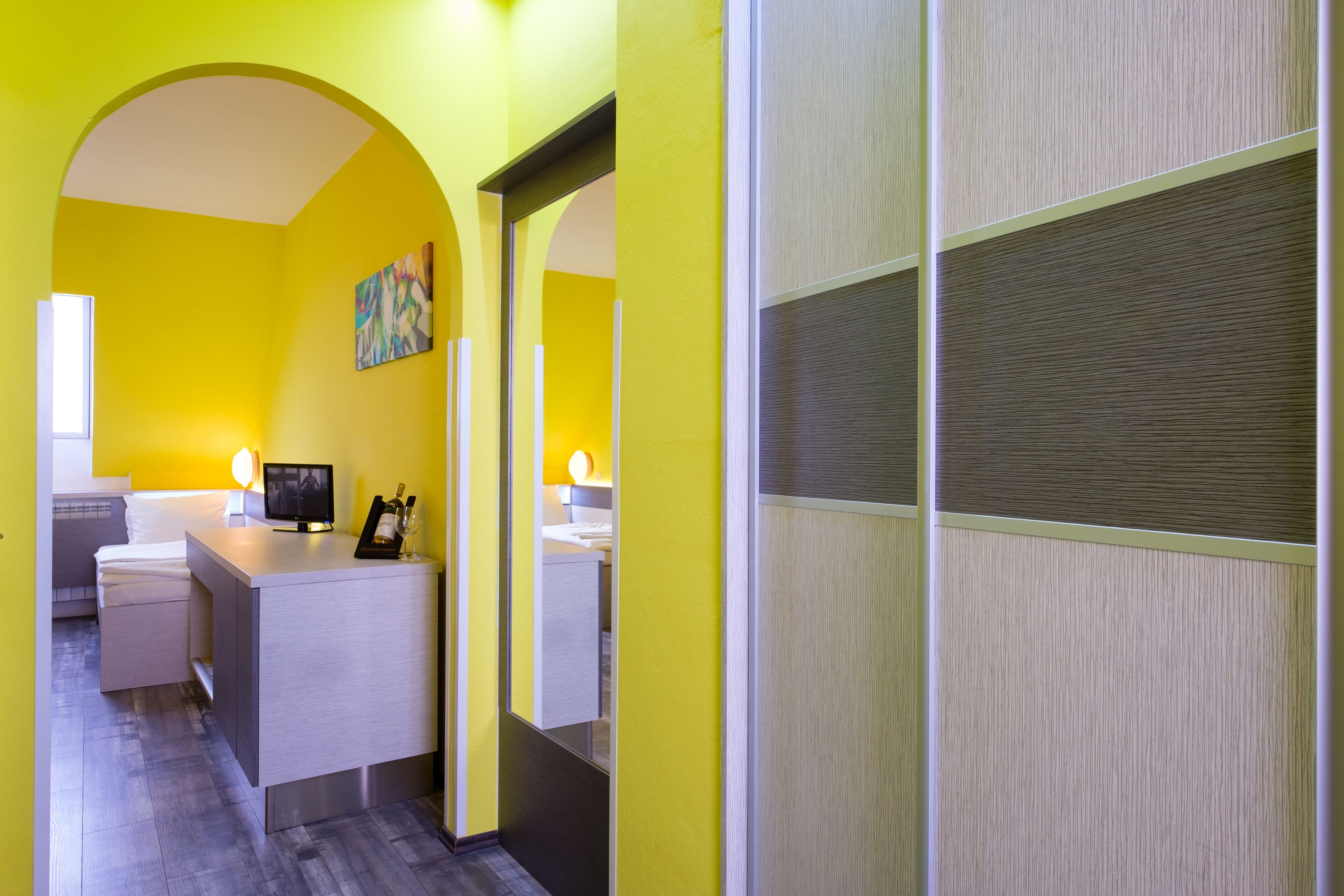 A hotel room with a bright yellow wall, a small desk with a television, and a bed.