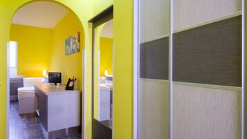 A hotel room with a bright yellow wall, a small desk with a television, and a bed.