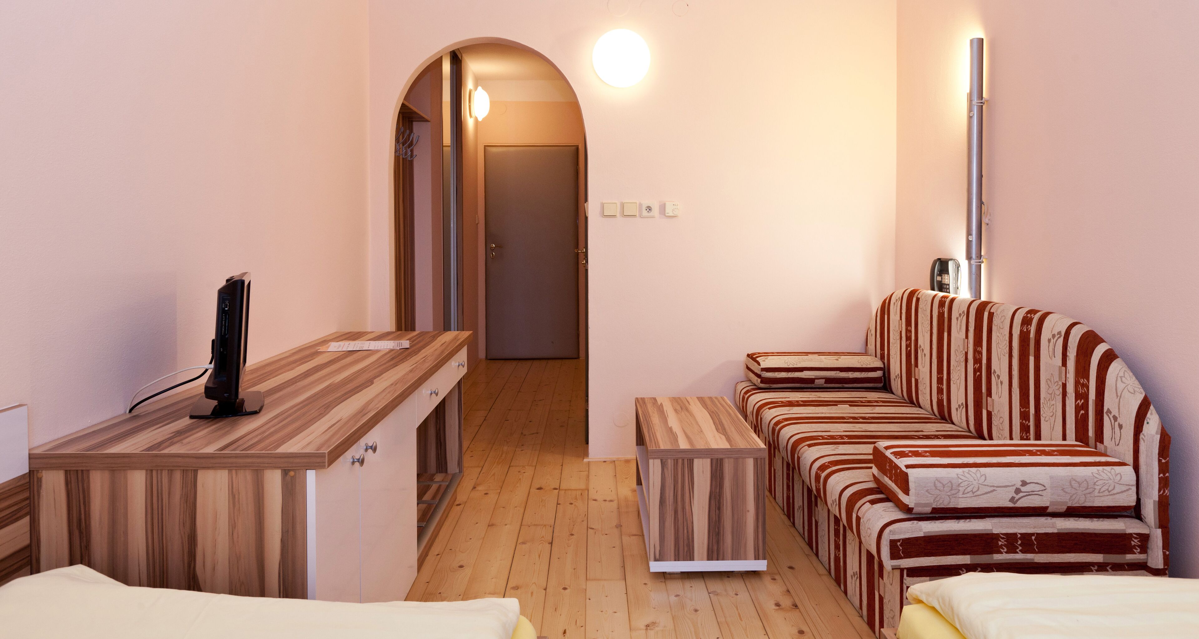 A compact room with a wooden desk, a striped sofa, and a small bedside table.